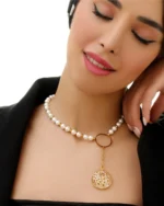 Close-up of a handmade pearl necklace with a golden chain and round pendant filled with tiny real dried flowers in resin, worn by a woman with closed eyes and natural makeup