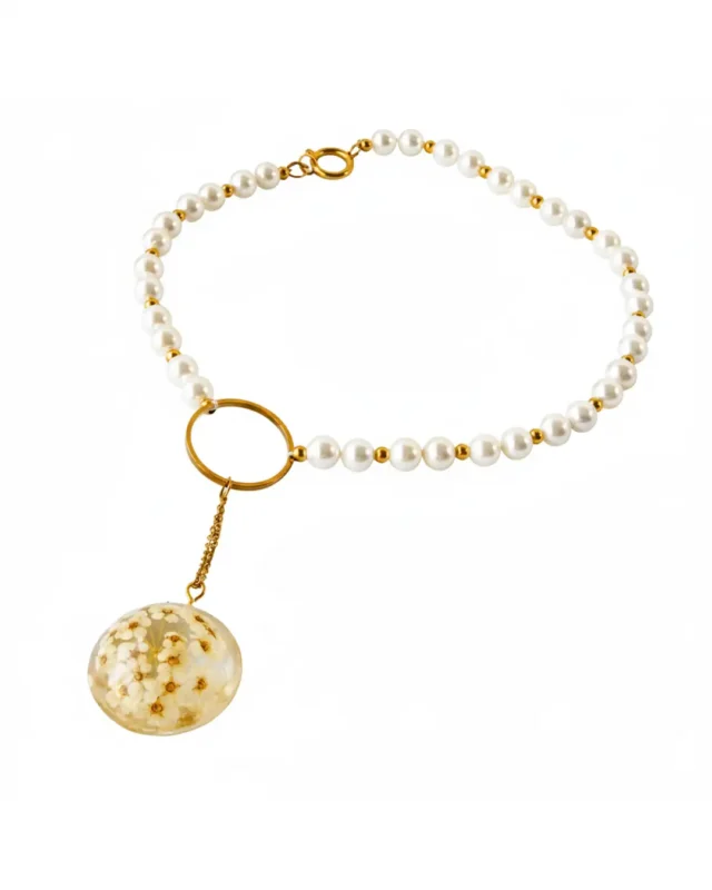 A pearl choker necklace featuring white beads and gold accents, with a round resin pendant containing delicate preserved white flowers