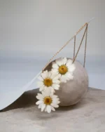 Close-up of a handmade triple daisy cascade necklace featuring three real white daisies preserved in resin, arranged vertically on a delicate gold chain, displayed on a stone sphere with soft studio lighting.
