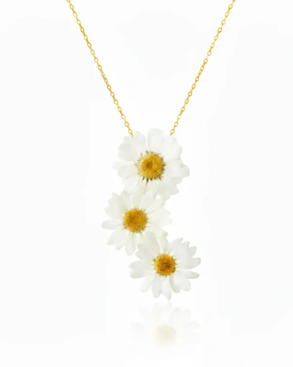 A delicate necklace featuring three real white daisy flowers arranged in a vertical cascade on a fine gold chain, set against a clean white background