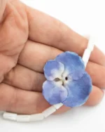 Close-up of handmade bracelet with real blue hydrangea flower preserved in UV resin, combined with tubular white shell beads