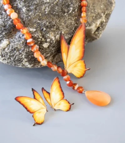 Handmade butterfly jewelry set with orange wing necklace and matching earrings, designed with natural carnelian gemstone beads and teardrop pendant, displayed on stone