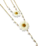 A delicate gold-chain necklace featuring two real pressed daisy flowers, accented with small white pearls and a dangling teardrop pearl, displayed on a white background