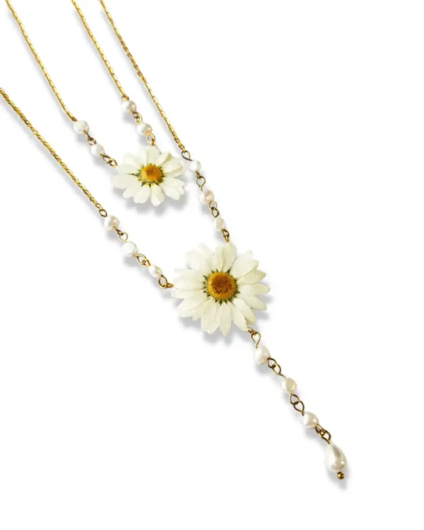 A delicate gold-chain necklace featuring two real pressed daisy flowers, accented with small white pearls and a dangling teardrop pearl, displayed on a white background