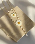 A natural daisy resin necklace with a gold chain and pearl beads, displayed on a textured stone surface under soft sunlight.