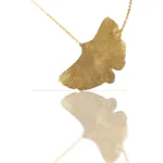 Handmade ginkgo leaf necklace with gold chain, nature-inspired jewelry piece reflecting light on white background