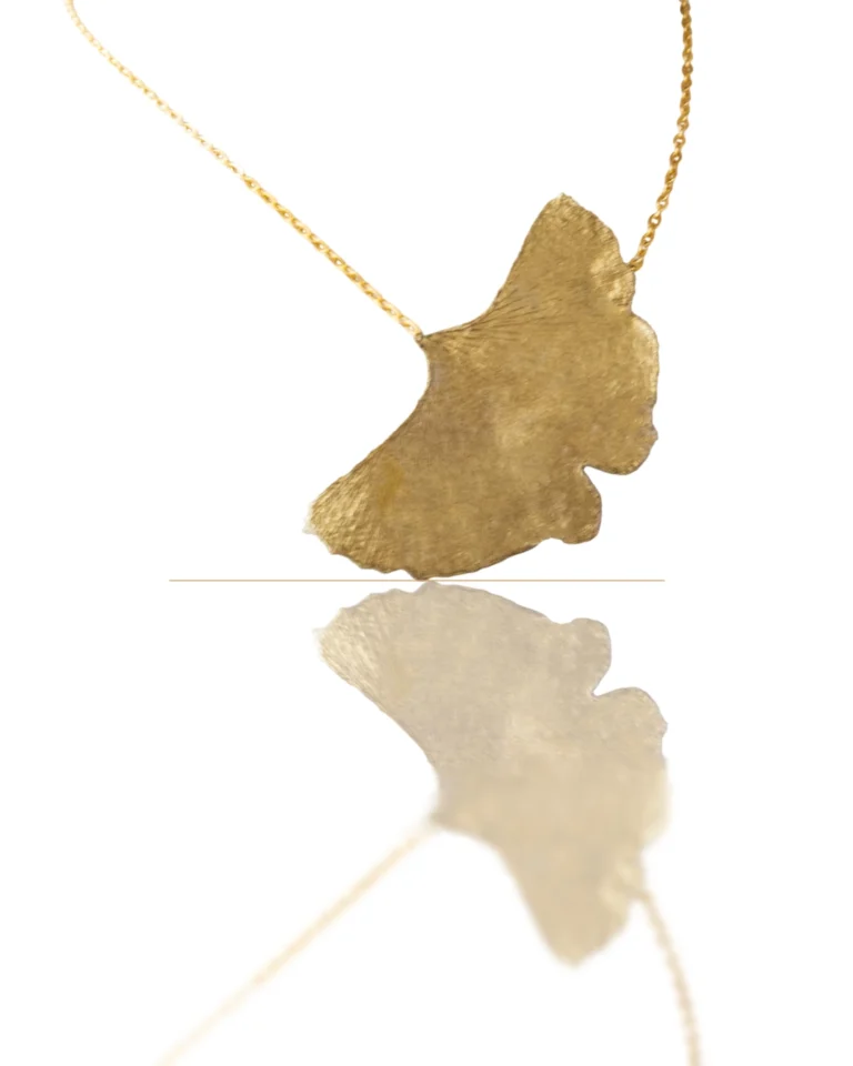 Handmade ginkgo leaf necklace with gold chain, nature-inspired jewelry piece reflecting light on white background