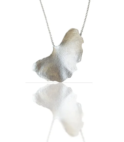Handmade ginkgo leaf necklace with silver chain, nature-inspired jewelry piece reflected on white surface