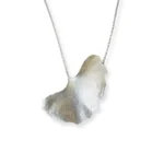 Handmade ginkgo leaf necklace with silver chain, nature-inspired jewelry piece reflected on white surface