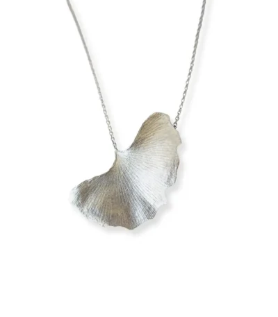 Handmade ginkgo leaf necklace with silver chain, nature-inspired jewelry piece reflected on white surface