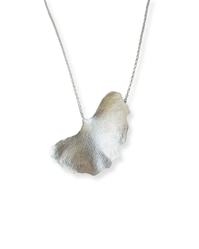 Handmade ginkgo leaf necklace with silver chain, nature-inspired jewelry piece reflected on white surface