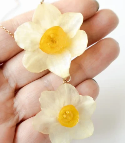 Close-up of handmade necklace with two real narcissus flowers preserved in UV resin, held in hand, delicate nature-inspired jewelry