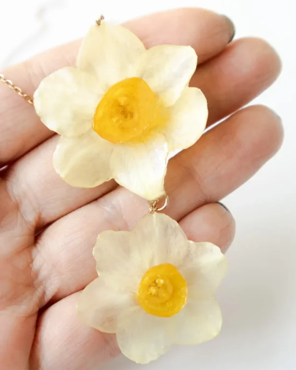 Close-up of handmade necklace with two real narcissus flowers preserved in UV resin, held in hand, delicate nature-inspired jewelry