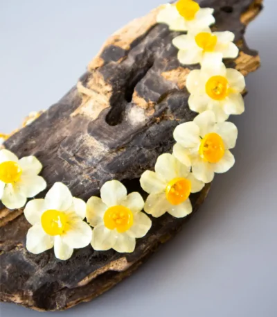 Handmade choker necklace with real narcissus flowers preserved in UV resin, displayed on wooden background, nature-inspired jewelry design