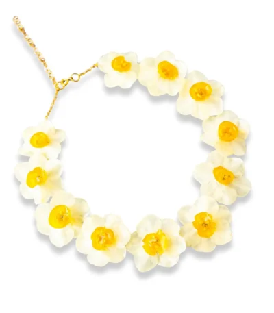 A delicate layered gold necklace featuring two real pressed daisy flowers and small white pearls, displayed on a soft beige fabric with natural light and floral shadows.