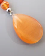 Close-up of orange teardrop pendant made from natural carnelian gemstone, part of handmade butterfly necklace design