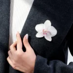 Handmade brooch with a real white orchid flower coated in UV resin, worn on a dark wool coat for an elegant and natural look