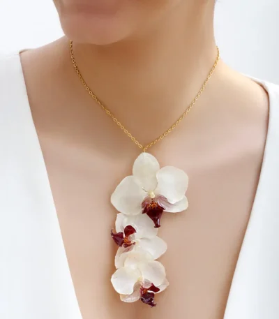 Handmade necklace featuring cascading real white orchid flowers with purple centers, preserved in UV resin, on a delicate gold chain, shown worn on model’s neck