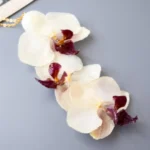 Close-up of a handmade necklace with cascading real orchid flowers in white and purple tones, preserved in UV resin, attached to a delicate gold chain, displayed on a gray surface