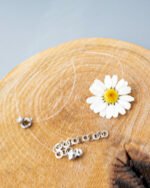 Handmade necklace with a real daisy flower encased on a transparent cord, displayed on a wooden surface with silver clasp and extender