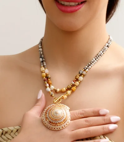 Handmade necklace with large natural seashell pendant and gemstone beads, worn by model with hand on chest, boho-inspired jewelry design