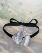 Handmade silver hydrangea petal choker with a black ribbon displayed on soft fabric with a dreamy floral background
