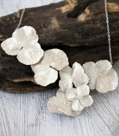 Close-up of a handmade necklace featuring multiple real hydrangea petals coated with silver leaf and UV resin, displayed on a rustic wooden background with a silver chain