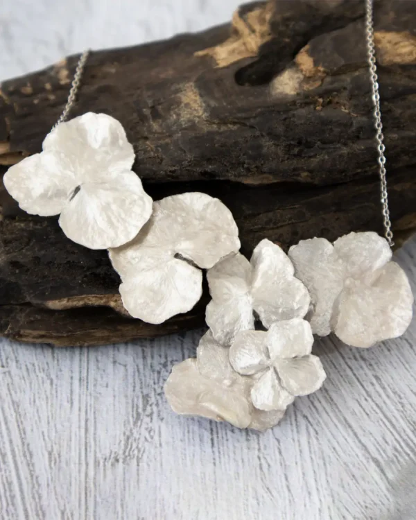 Close-up of a handmade necklace featuring multiple real hydrangea petals coated with silver leaf and UV resin, displayed on a rustic wooden background with a silver chain