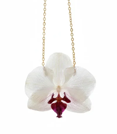 A delicate white orchid flower preserved in clear resin, hanging from a fine gold chain against a clean white background.